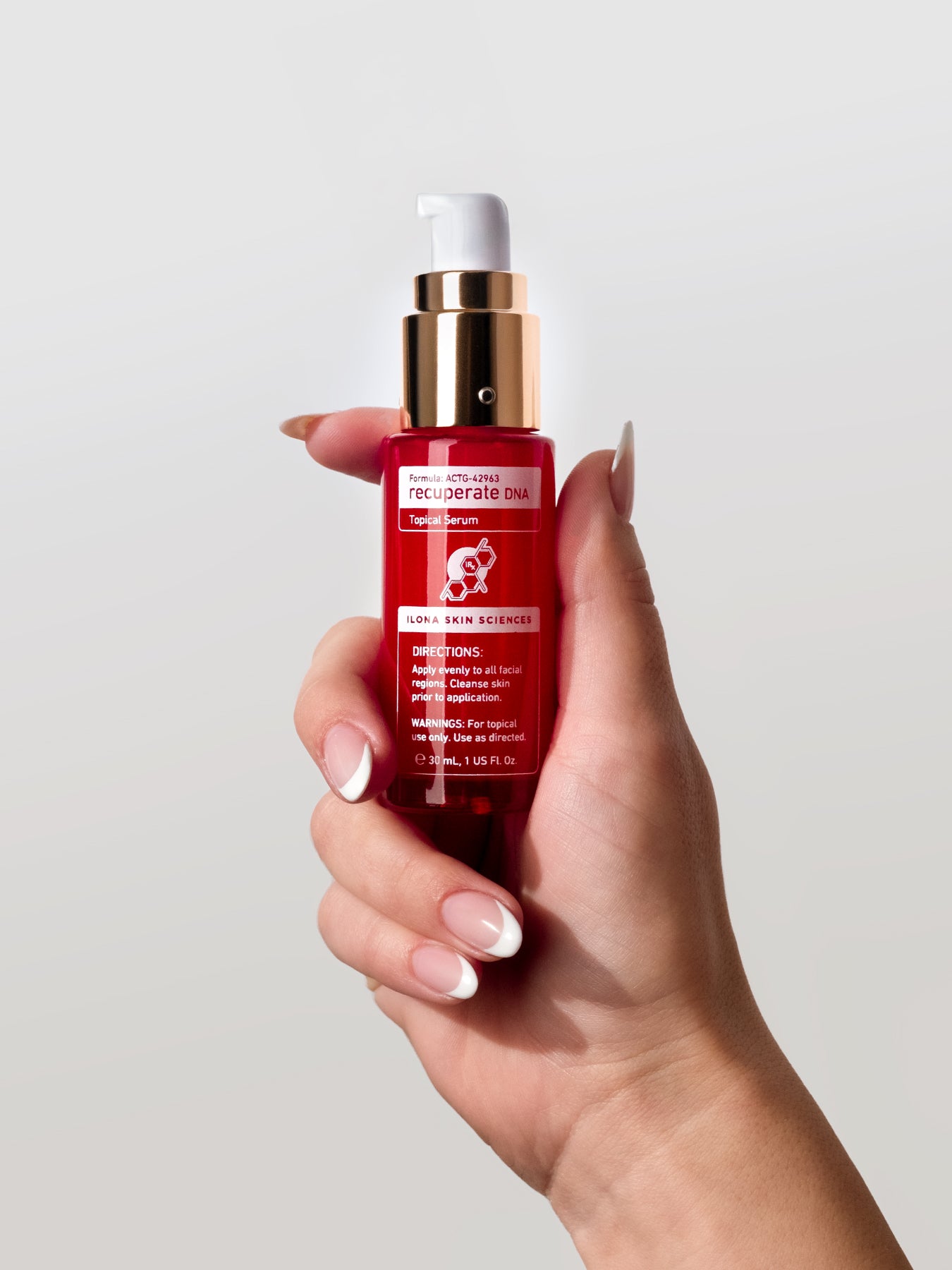 Hand holding a red skincare bottle with a white cap against a light gray background